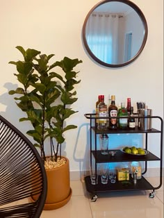 a bar cart with liquor bottles and drinks on it next to a potted plant