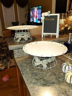 two cake stands sitting on top of a kitchen counter next to a tv screen and pumpkins