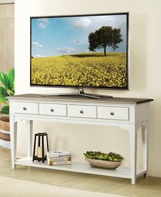 a flat screen tv sitting on top of a white table next to a plant in a vase