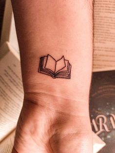 a small tattoo on the wrist of a person with a book in it's hand