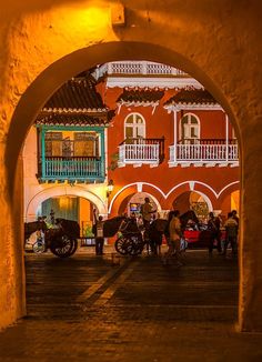 an archway leading into a building with people walking around it and horse drawn carriages on the street