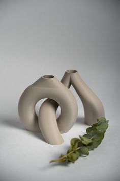 two grey vases sitting next to each other on a white surface with green leaves