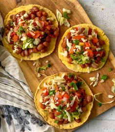 three tortillas topped with tomatoes, lettuce and other toppings on a wooden cutting board