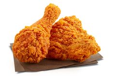 two pieces of fried chicken sitting on top of brown tissue paper next to each other