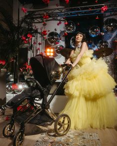 a woman in a yellow dress is standing next to a baby stroller and balloons