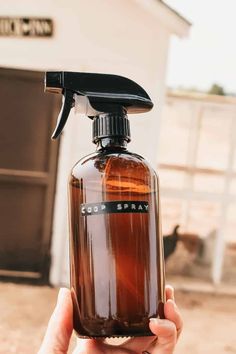 someone holding up a brown spray bottle in front of a horse barn with a black top