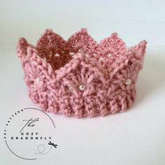 a crocheted pink crown sits on a white surface