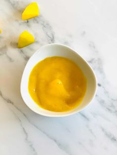 a white bowl filled with yellow liquid next to cut up pieces of lemons on a marble surface