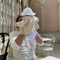 a man holding a baby up to his face while sitting on a chair in front of a table