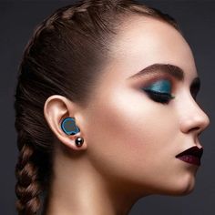 a woman with blue eyeshades and black eyeliners is wearing ear piercings