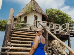 a woman in a blue dress is standing on the steps leading to a small house