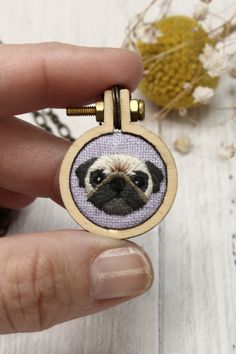 a hand holding a small embroidered keychain with a pug face on it