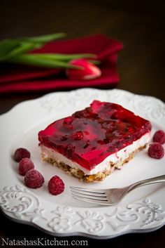 a piece of cake with raspberry topping on a plate next to some flowers