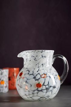 a marbled glass pitcher sitting on top of a table next to two orange cups