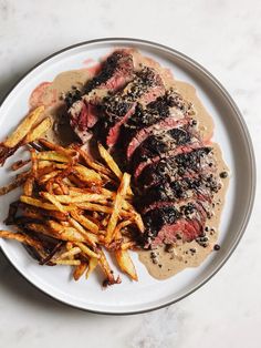 steak and french fries on a white plate with brown gravy over it, sitting on a marble surface