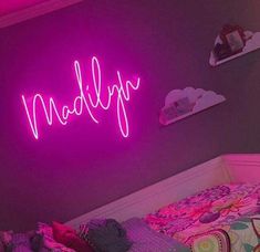 there is a neon sign that says madly on the wall above a bed with pillows and blankets