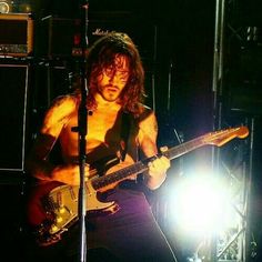 a shirtless man with long hair playing guitar in front of a microphone and amp