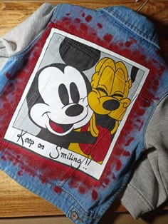 a mickey mouse jacket with the words keep on smiling printed on it, sitting on top of a wooden surface