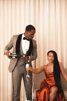 a man in a tuxedo pouring champagne into a woman's dress sitting on a couch