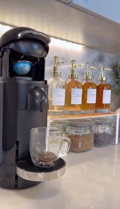 a coffee maker sitting on top of a counter next to some jars and cups filled with liquid