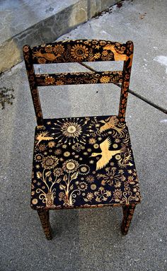 an old wooden chair sitting on the side of a street next to a sidewalk with flowers and birds painted on it