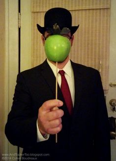 a man in a suit and top hat holding an apple on a stick to his face