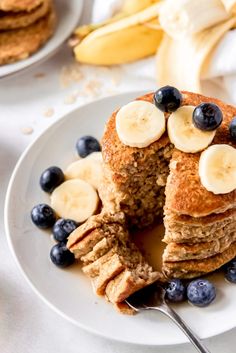 a stack of pancakes with blueberries and bananas cut in half on a white plate