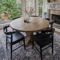 a dining room table with four chairs and a vase on top of it in front of a fireplace