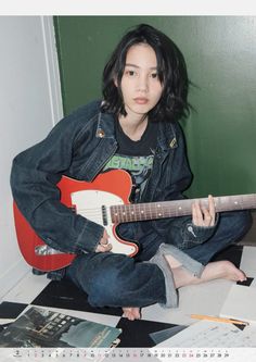 a young woman sitting on the floor with an electric guitar in her lap and looking at the camera