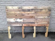 a wooden bench made out of old pallets sitting in front of a brick wall