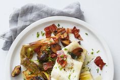 a white plate topped with fish, artichokes and bacon next to a fork