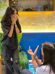 two women sitting down and one is covering her face with her hands while the other holds her hand up to her mouth