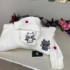 two white sweatshirts with stitching on them sitting on a table next to flowers