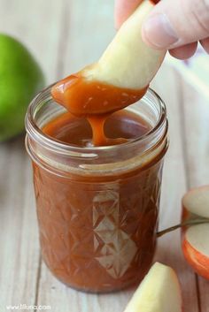 someone dipping an apple into a jar of homemade caramel apple dip