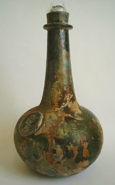 an old vase with some paint on it sitting on a white table top next to a wall