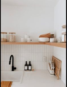 a white kitchen with wooden shelves and dishes on the shelf above the sink is full of utensils