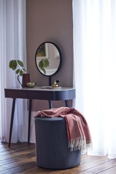 a round mirror sitting on top of a table next to a black stool with a red blanket