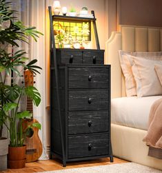 a black chest of drawers sitting in front of a bed next to a potted plant