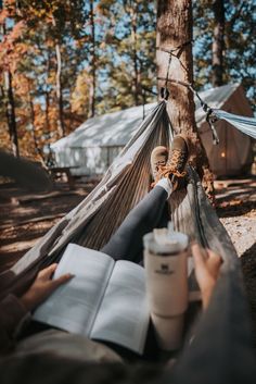 a person laying in a hammock reading a book and holding a coffee cup