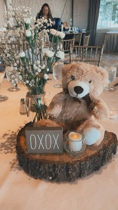 a brown teddy bear sitting on top of a wooden table next to a vase filled with flowers