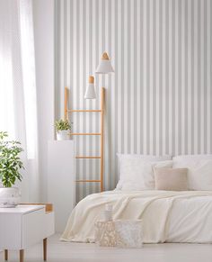 a bedroom with striped wallpaper and white bedding in front of a planter