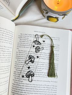 an open book with some tassels on top of it next to a candle