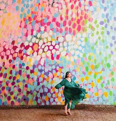 a woman in a green dress is dancing near a colorful wall with circles on it