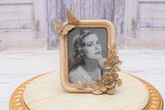 a photo frame with a flower and butterfly decoration on top of a wooden table next to a wall