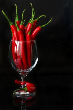 a glass filled with red peppers sitting on top of a table