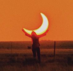 a person standing in a field with their arms out and the sun shining behind them