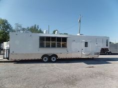 a white trailer parked in a parking lot next to other vehicles and trees on a sunny day