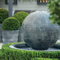 a water fountain surrounded by bushes and potted plants