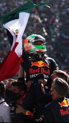 a red bull driver is holding the flag in his hand and some people are looking on