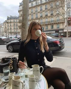 a woman sitting at an outdoor table drinking from a cup